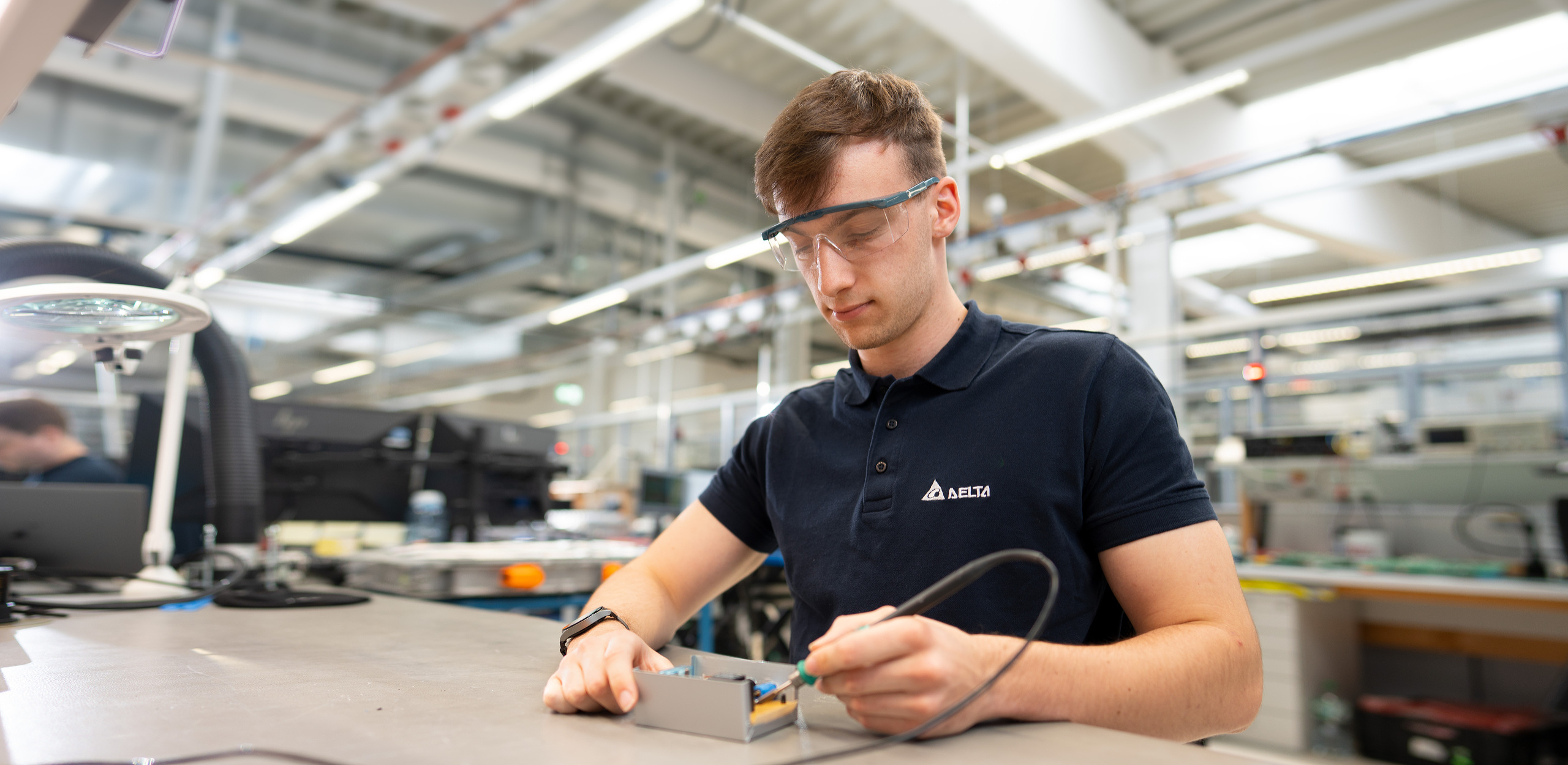 Junger Student lötet ein Bauteil und trägt eine Schutzbrille.
