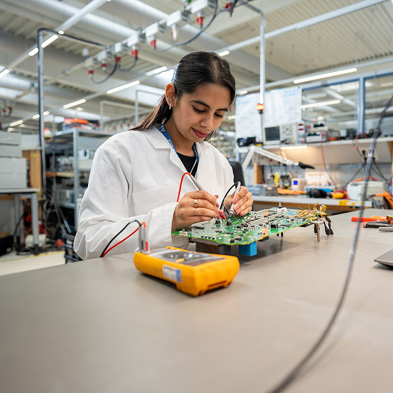 Junge Frau überprüft mit einem Multimeter ein Bauteil