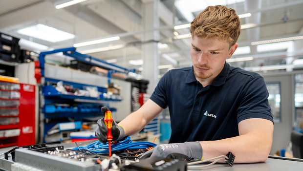 Ein Student überprüft ein großes Bauteil mit vielen verschiedenen Stromkabeln.