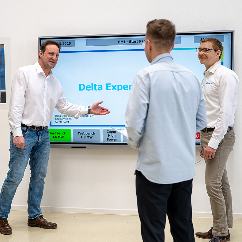 Drei Männer unterhalten sich und einer von ihnen zeigt etwas auf einem Touch-Display.