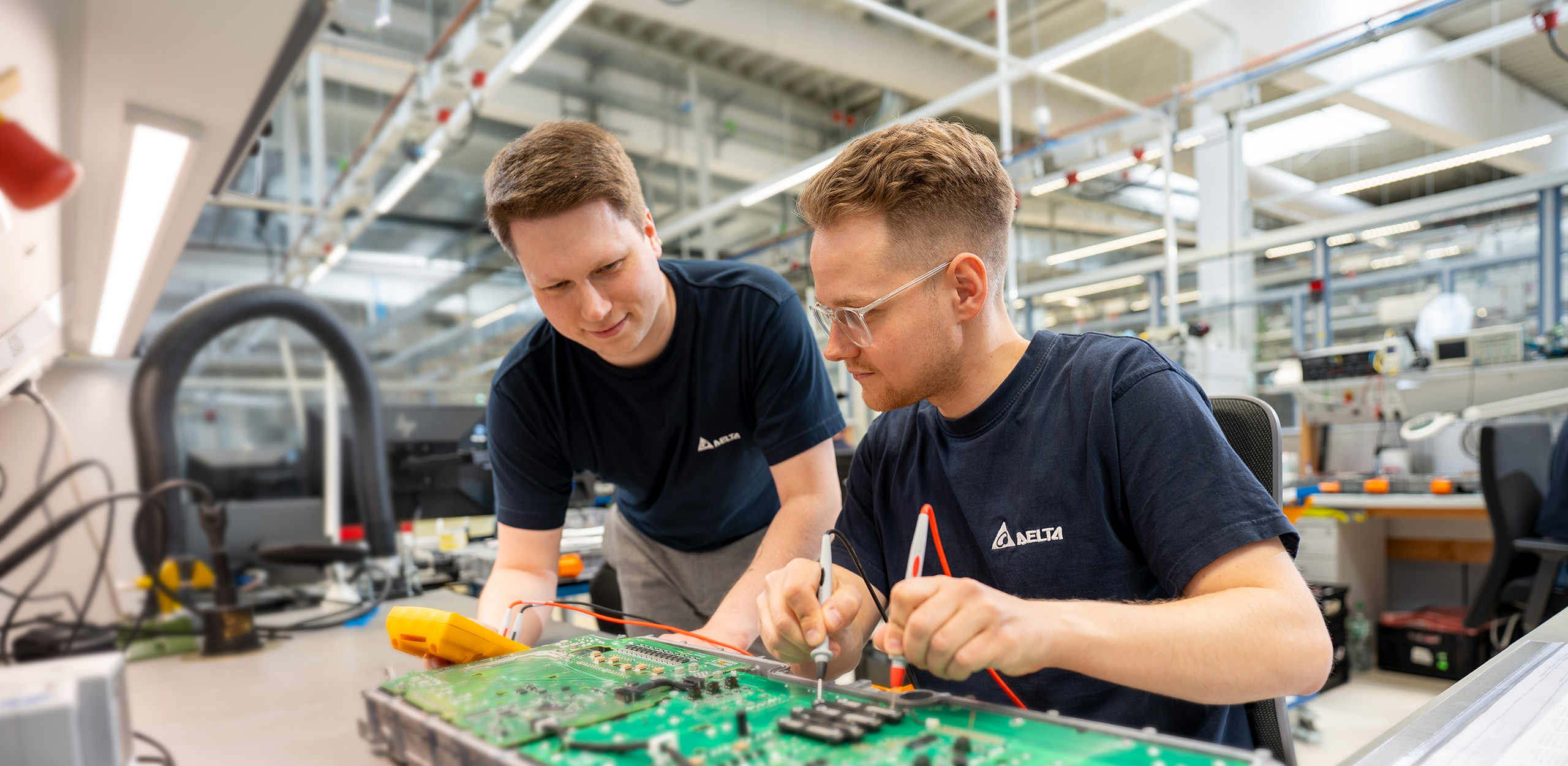 Two young men are inspecting a product with a soldering iron that is placed on the table in front of them