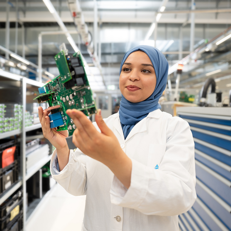 A young woman wearing a headscarf is inspecting a component in development