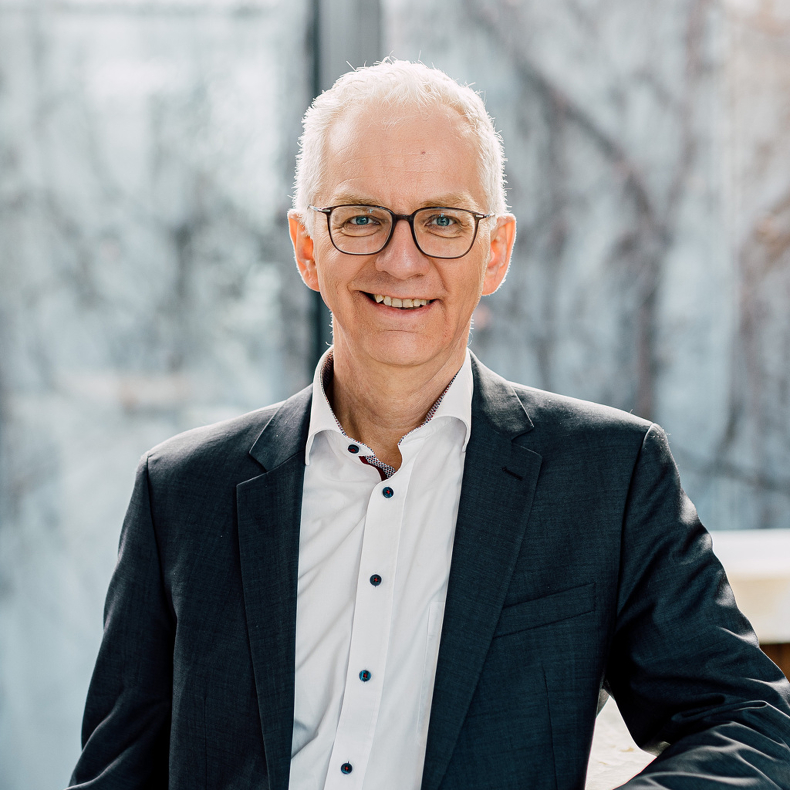 Peter Ide A middle-aged man with glasses is wearing a black suit with a white shirt