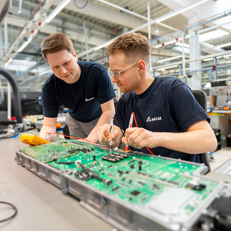 Two young men are inspecting a product with a soldering iron that is placed on the table in front of them
