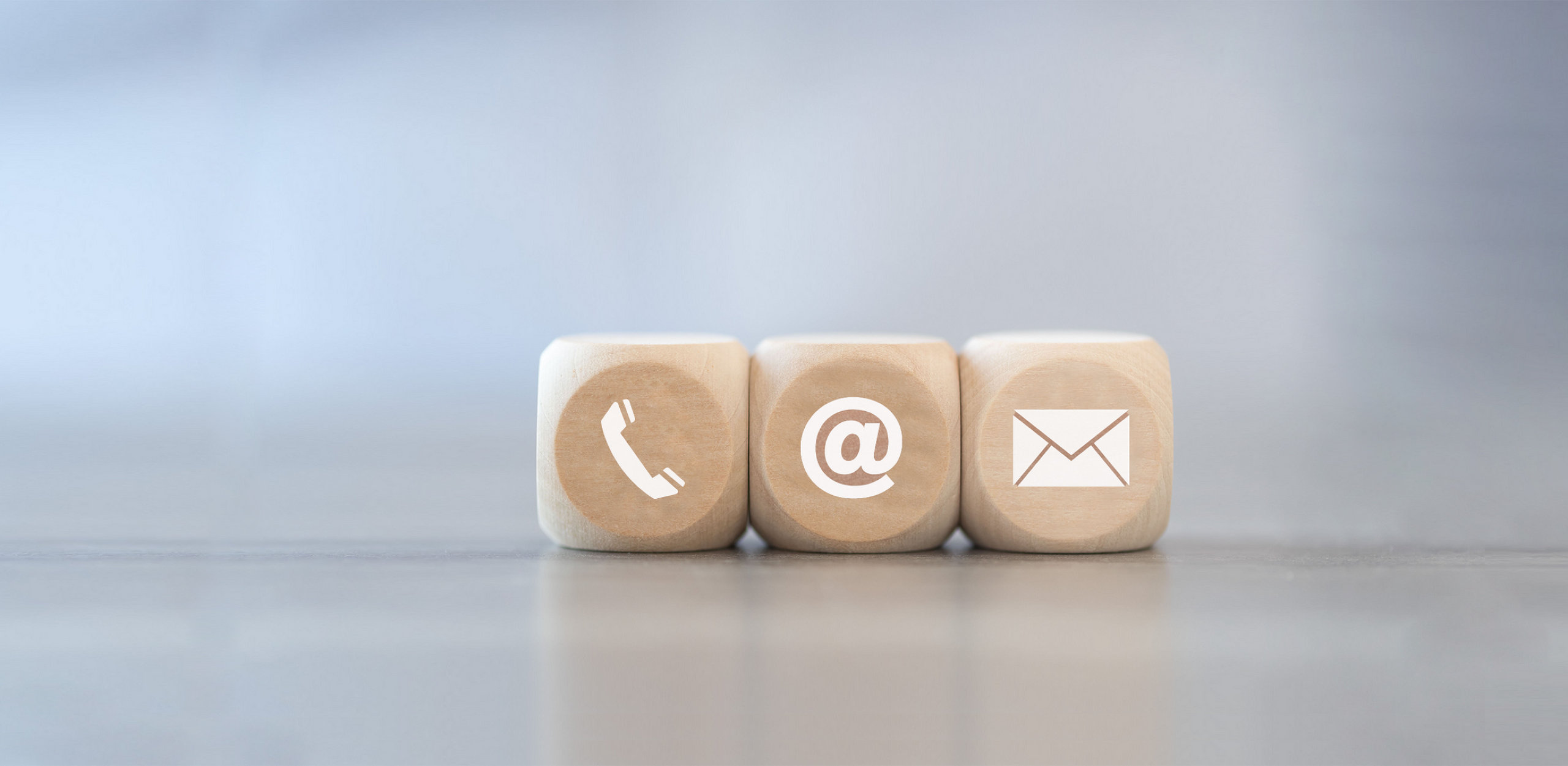 Three wooden cubes, each displaying a different contact symbol: a telephone handset, an @ symbol, and an envelope, representing various ways to get in touch